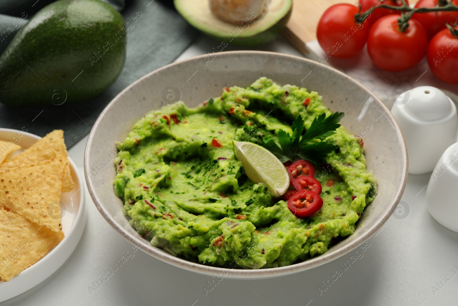 Photo of Delicious guacamole with nachos chips and ingredients on white table