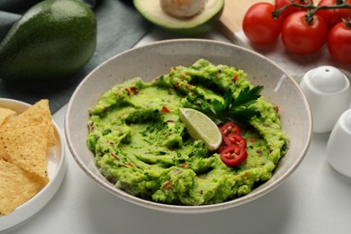 Delicious guacamole with nachos chips and ingredients on white table