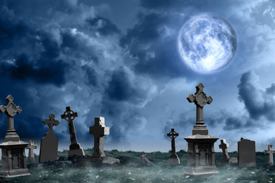 Misty graveyard with old creepy headstones under full moon on Halloween
