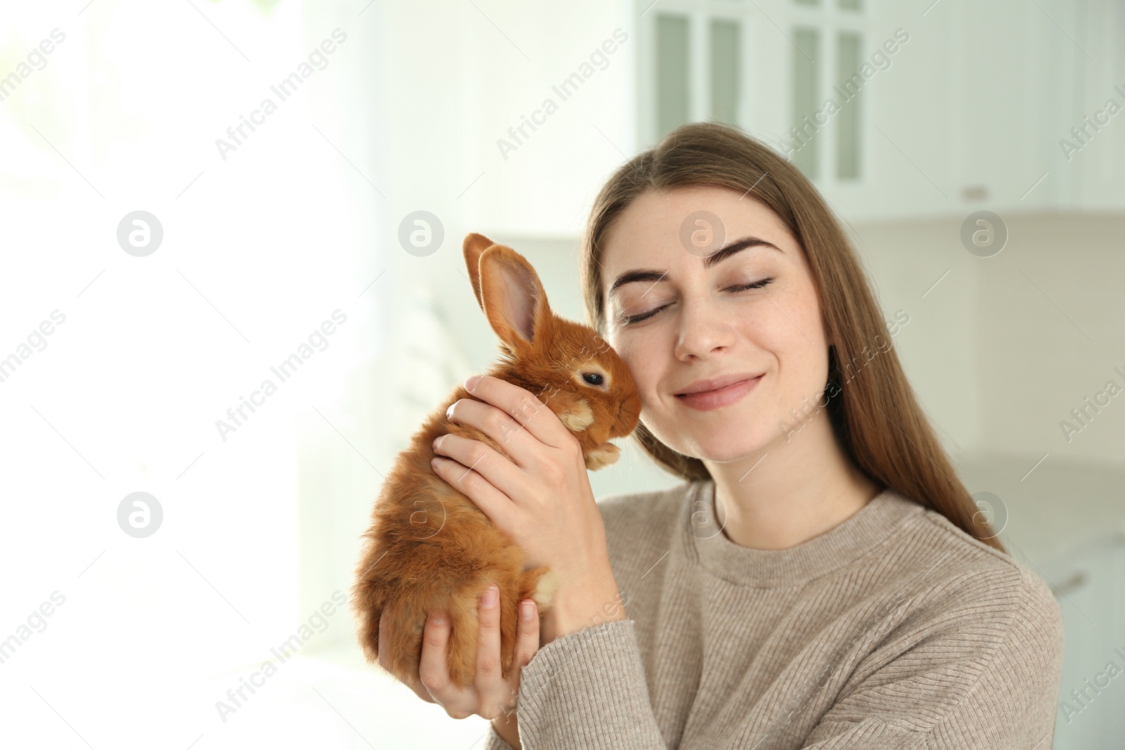 Photo of Young woman with adorable rabbit indoors. Lovely pet