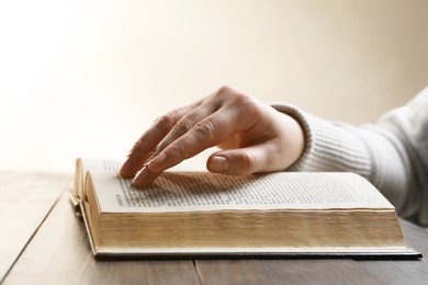 Photo of Woman reading Bible at wooden table, closeup