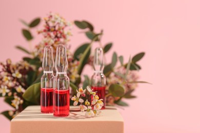 Photo of Stylish presentation of skincare ampoules and flowers on pink background, closeup. Space for text