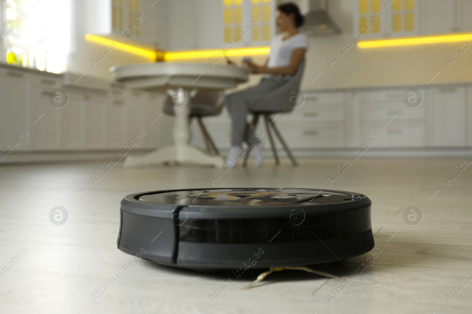 Photo of Modern robotic vacuum cleaner and blurred woman on background