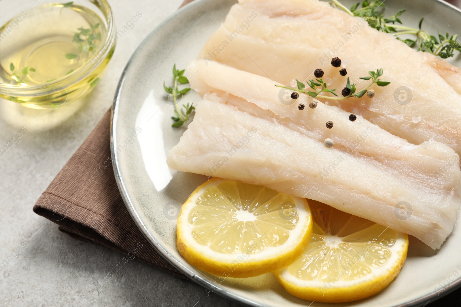 Photo of Plate with raw cod fish, spices, microgreens and lemon on grey table, closeup