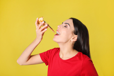 Beautiful woman eating tasty pizza on yellow background