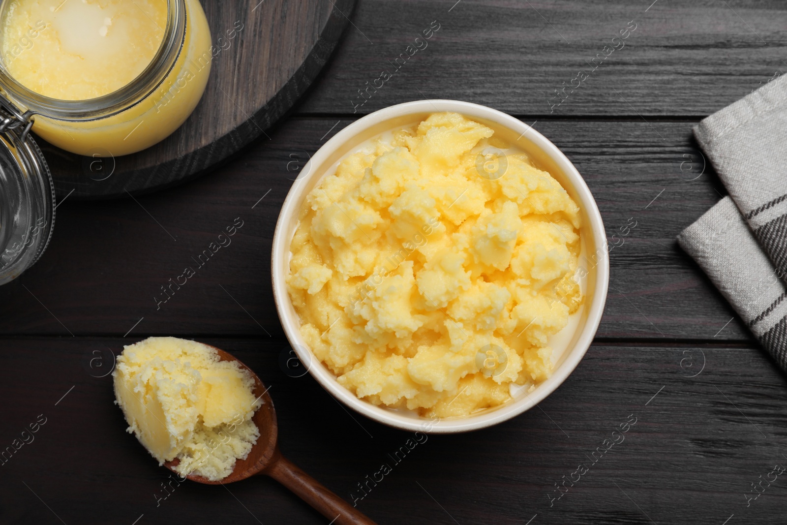 Photo of Ghee butter in dishware on wooden table, flat lay