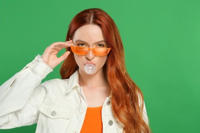 Photo of Beautiful woman in sunglasses blowing bubble gum on green background. Space for text
