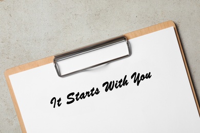 Clipboard with phrase It Starts With You on grey table, top view