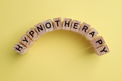 Photo of Wooden blocks with word HYPNOTHERAPY on yellow background, flat lay