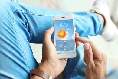 Man using weather forecast app on smartphone indoors, closeup