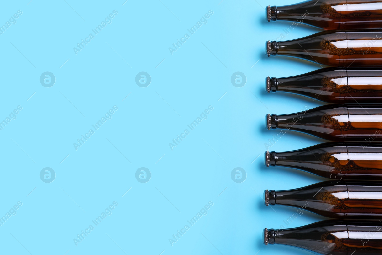 Photo of Bottles of beer on light blue background, flat lay. Space for text