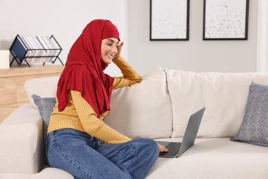 Photo of Muslim woman using laptop at couch in room