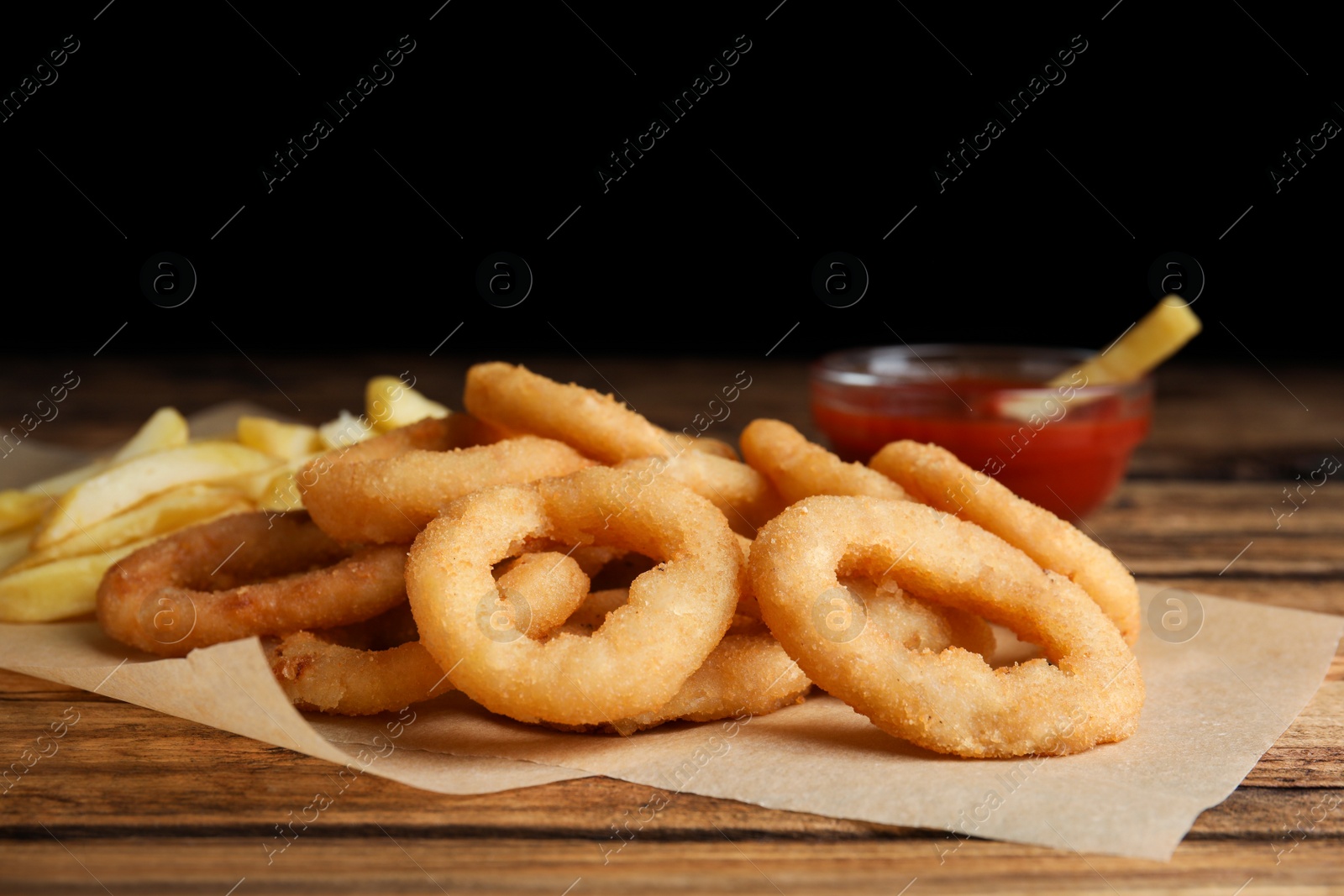 Photo of Delicious onion rings, fries and ketchup on wooden table, closeup