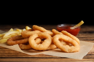 Photo of Delicious onion rings, fries and ketchup on wooden table, closeup