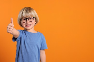 Cute little boy wearing glasses on orange background, space for text