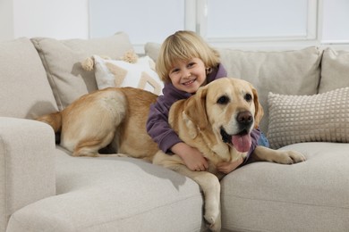 Photo of Cute little child with Golden Retriever on sofa at home. Adorable pet