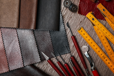 Photo of Leather samples and tools on brown table, flat lay
