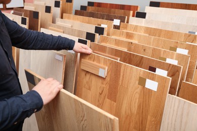 Photo of Man choosing wooden flooring among different samples in shop, closeup