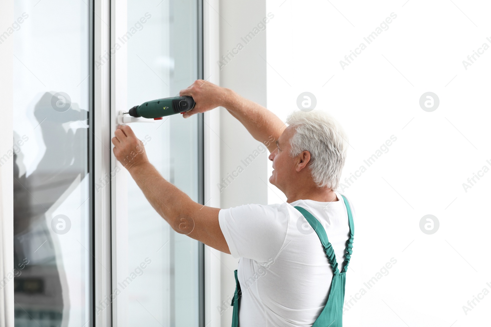 Photo of Mature construction worker repairing plastic window with electric screwdriver indoors