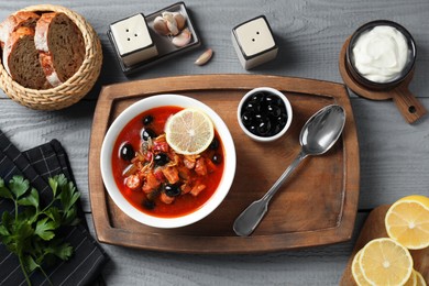 Photo of Meat solyanka soup with sausages, olives and vegetables served on grey wooden table, flat lay