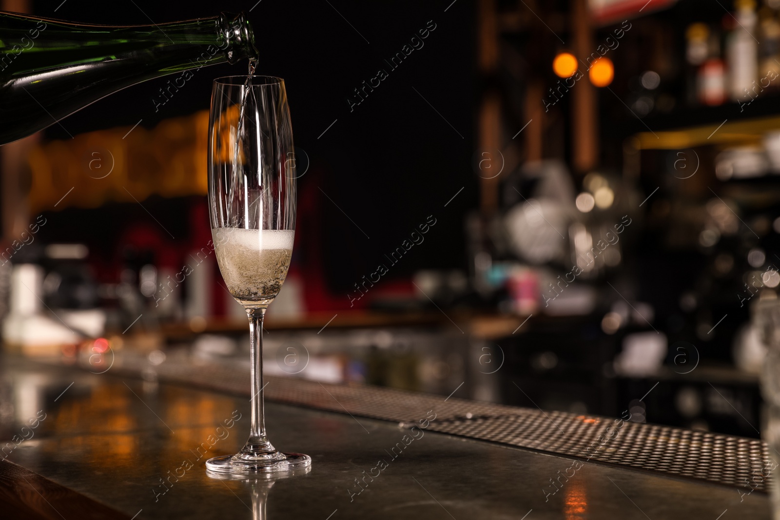 Photo of Pouring champagne from bottle into glass on counter in bar. Space for text