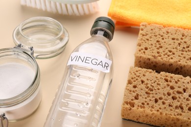 Photo of Eco friendly natural cleaners. Vinegar in bottle, jar of soda and sponges on beige background