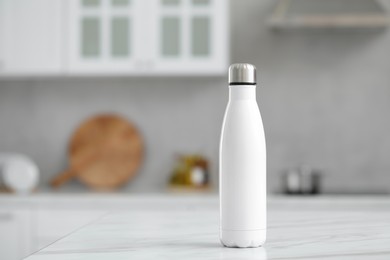 Photo of Stylish thermo bottle on white table in kitchen. Space for text