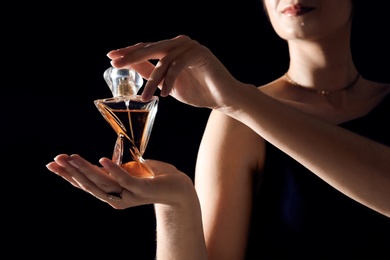Photo of Young woman with perfume bottle on black background, closeup