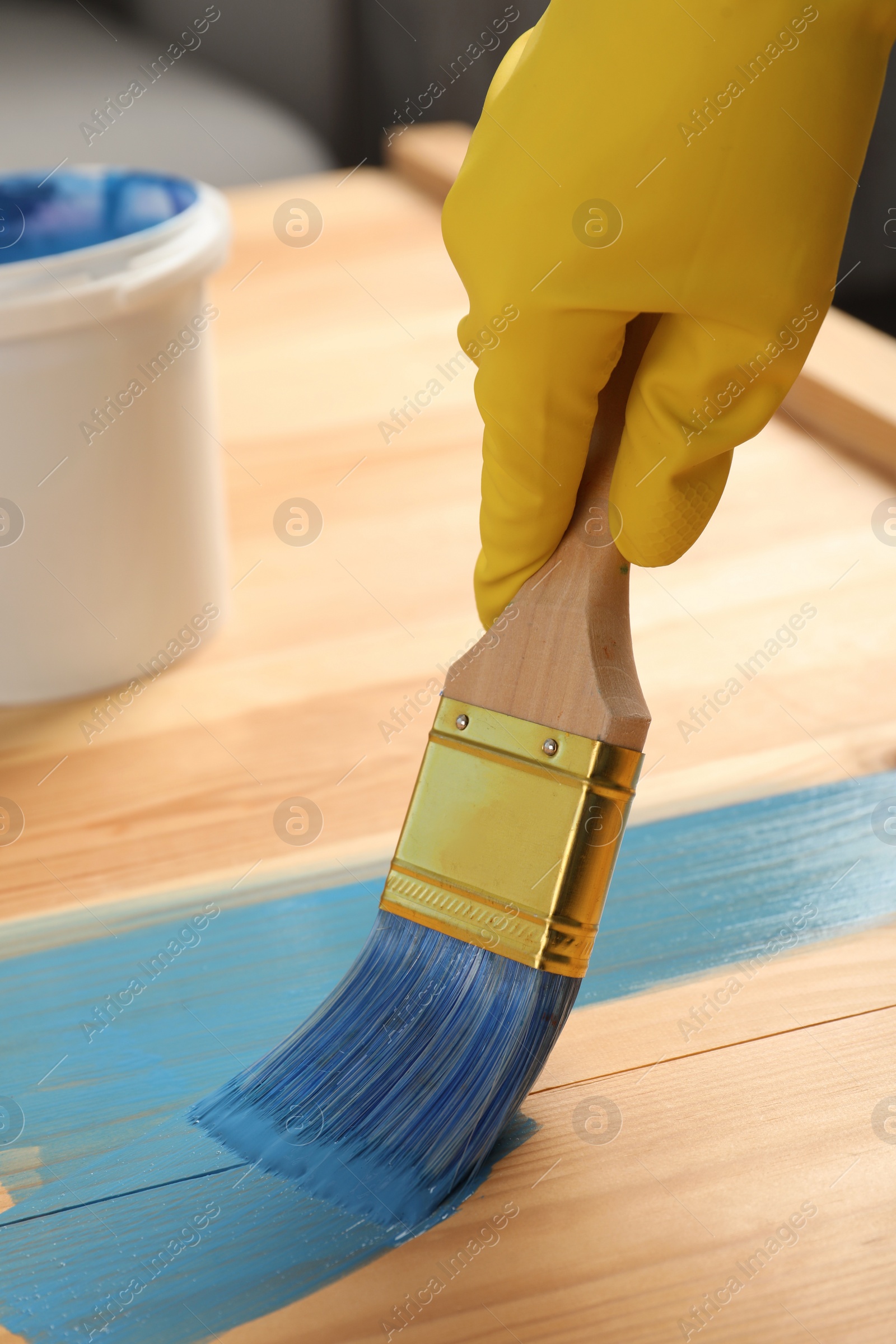 Photo of Worker applying blue paint onto wooden surface, closeup