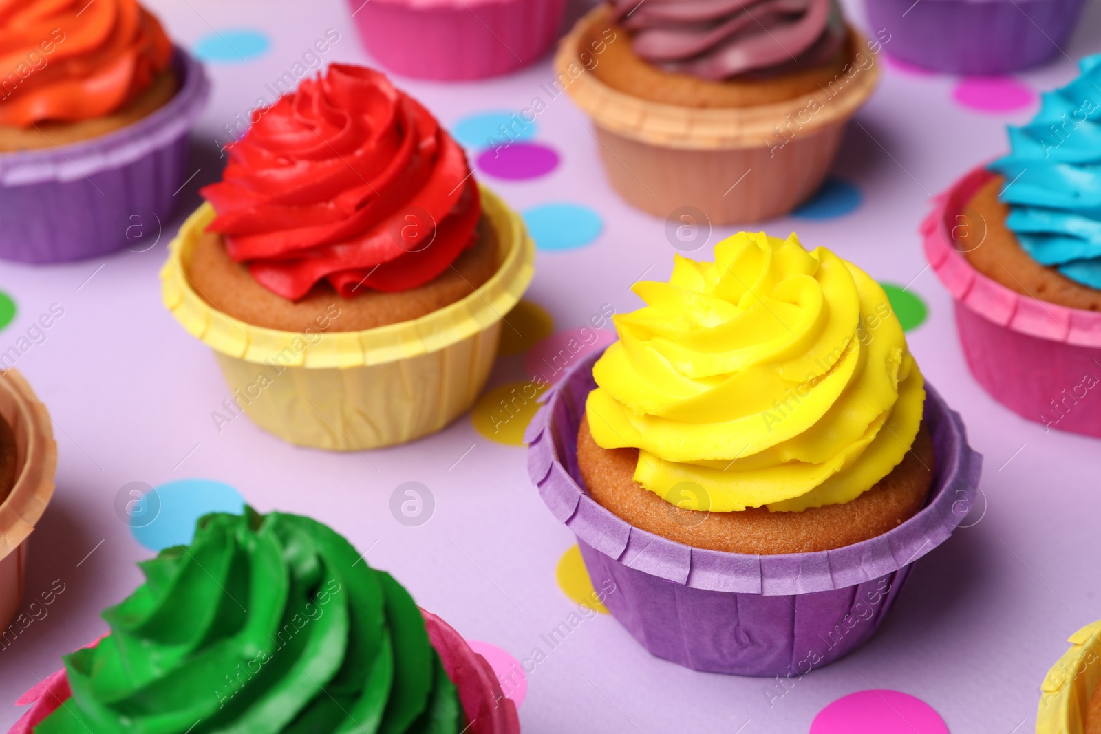Photo of Many delicious colorful cupcakes and confetti on violet background, closeup