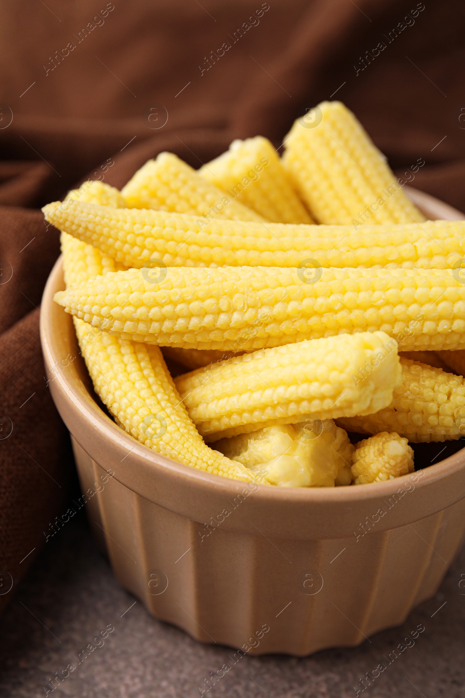 Photo of Tasty fresh yellow baby corns in bowl on brown table, closeup