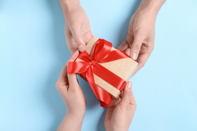 Photo of Man giving gift box to woman on light blue background, top view