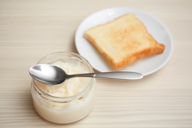 Photo of Jar with coconut oil and fresh toast on wooden background