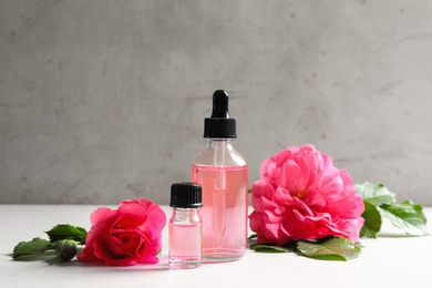 Photo of Fresh flowers and bottles of rose essential oil on white table