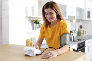 Woman checking blood pressure with sphygmomanometer at table indoors. Cardiology concept