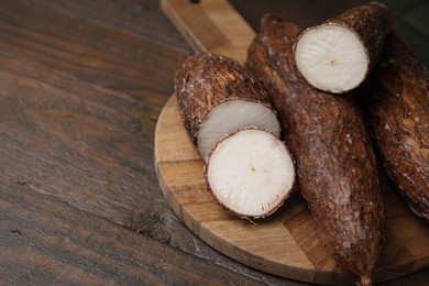 Photo of Whole and cut cassava roots on wooden table, closeup. Space for text