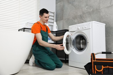 Photo of Young plumber repairing washing machine in bathroom, low angle view