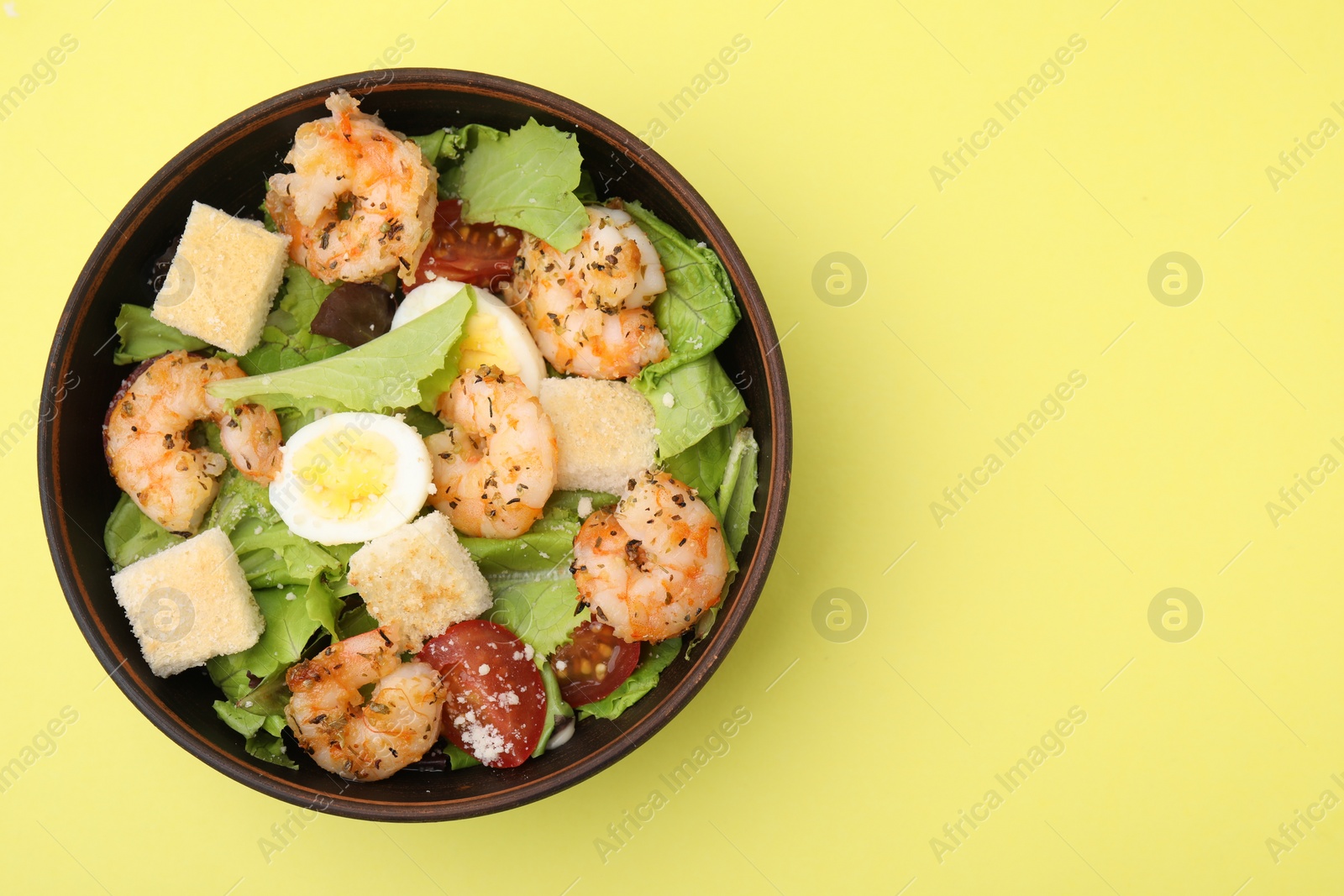 Photo of Delicious Caesar salad with shrimps on yellow background, top view. Space for text