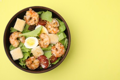 Photo of Delicious Caesar salad with shrimps on yellow background, top view. Space for text