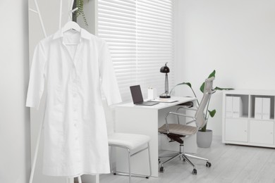 Doctor's gown on hanger near workplace in clinic