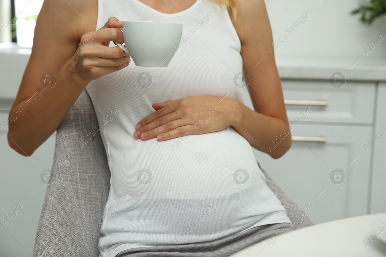 Photo of Beautiful pregnant woman drinking tea in kitchen, closeup