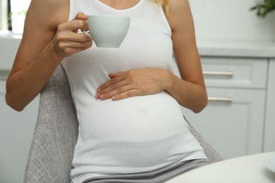 Beautiful pregnant woman drinking tea in kitchen, closeup