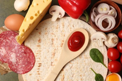 Photo of Pizza base, spoon with tomato sauce and products on green textured table, flat lay