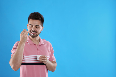 Photo of Happy young man eating tasty yogurt on light blue background. Space for text