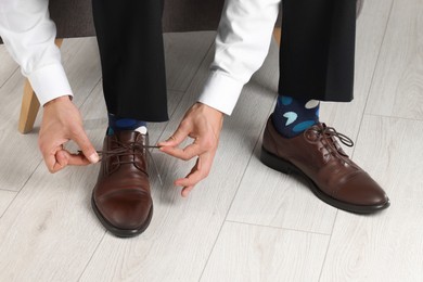 Man with colorful socks putting on stylish shoes indoors, closeup