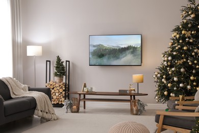 Modern TV set on light wall in room decorated for Christmas