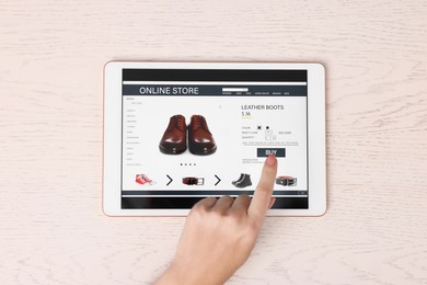 Photo of Woman with tablet shopping online at white wooden table, top view