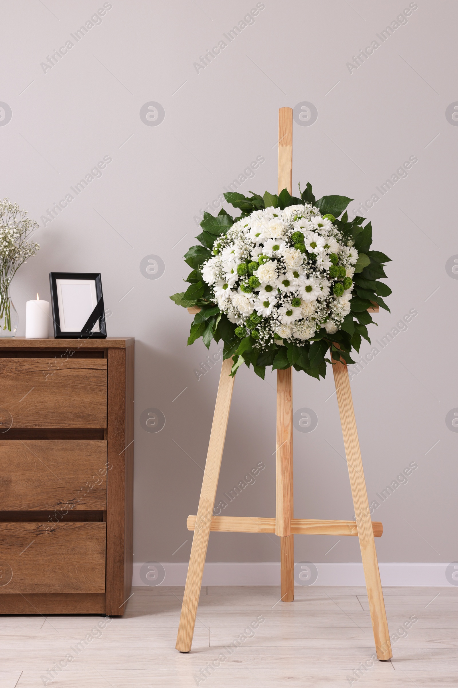 Photo of Wreath of flowers and frame with black ribbon on commode in room. Funeral attributes