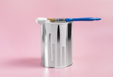 Photo of Can of white paint and brush on pink background