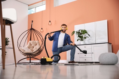 Young man having fun while vacuuming at home